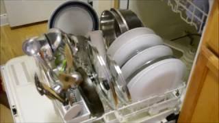 An open dishwasher correctly loaded with stainless steel Indian cookware and plates.
